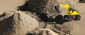 Ein gelber Sitzbagger auf einem Sandhaufen.