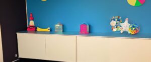 Ein Zimmer mit einer blauen Wand und einem weißen Schrank, dekoriert mit Babyspielzeug.