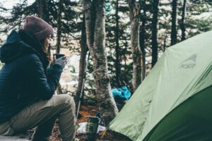 Eine Frau sitzt vor einem grünen Zelt im Wald.